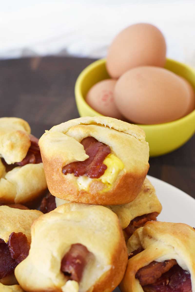 Bacon Egg and Cheese Crescent Bites made in a muffin tin. There are eggs in a yellow bowl in the shot to the right. 