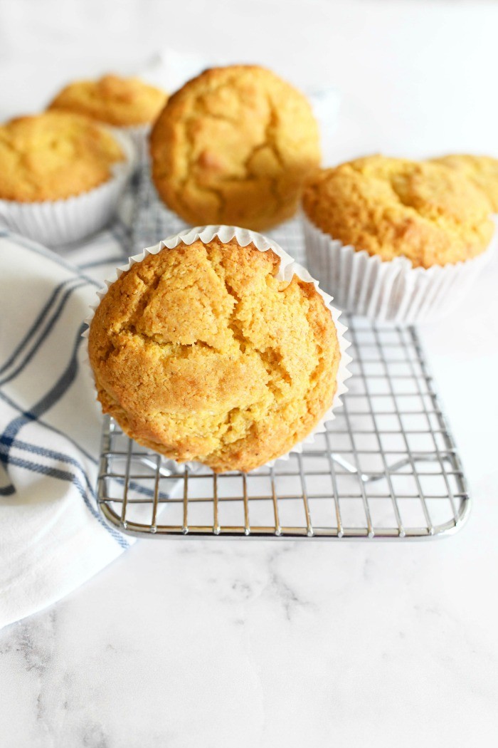 Bakery Style Jumbo Corn Muffins on a silver baking rack. There is a striped napkin in the shot as well.