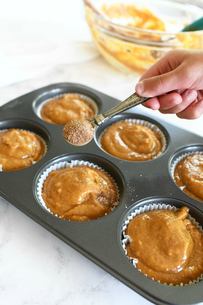 Bakery style pumpkin muffins batter. A hand is sprinkling cinnamon and sugar on these muffins.