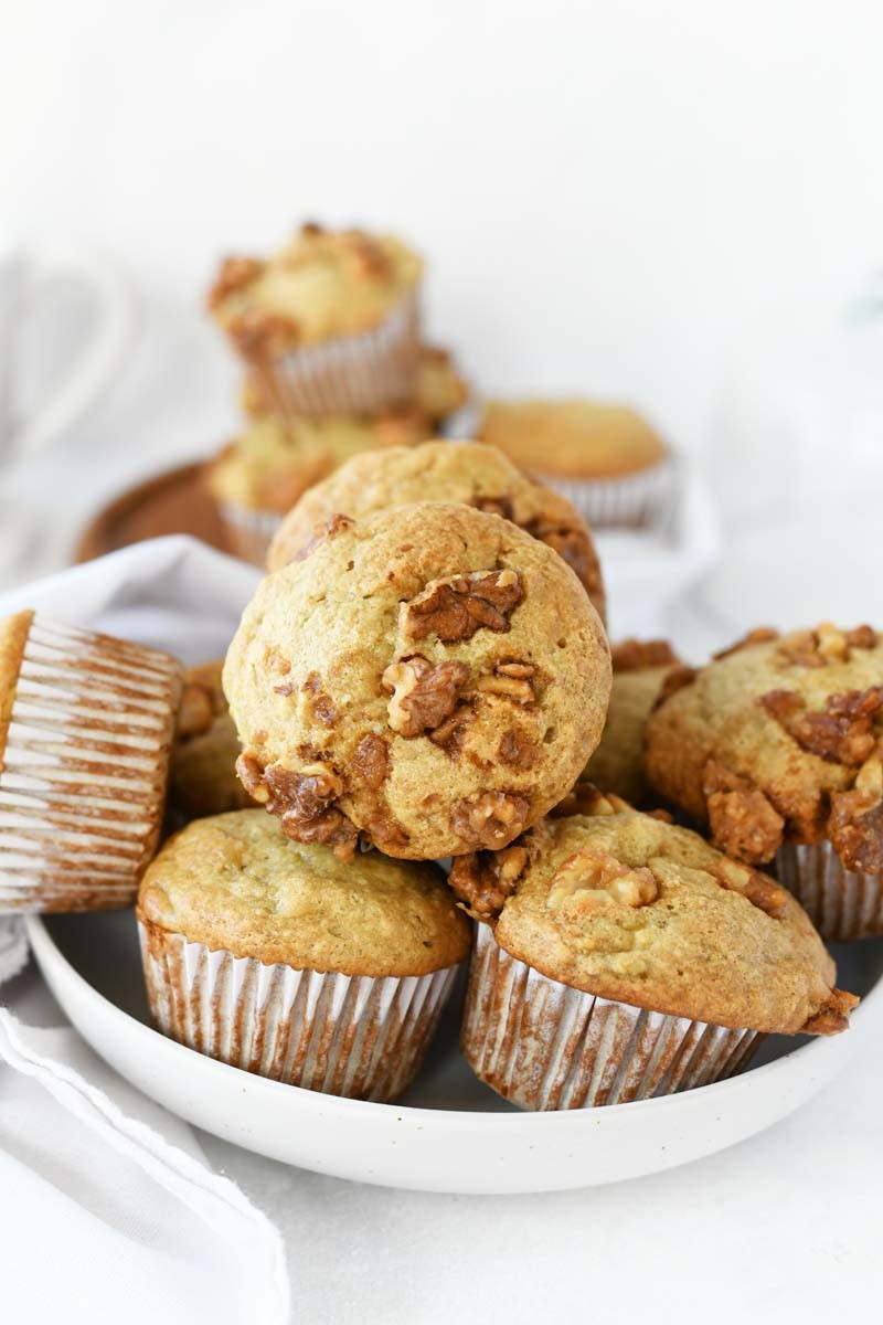 Banana Bread Muffins with Candied Walnuts stacked on top of each other on a white plate.