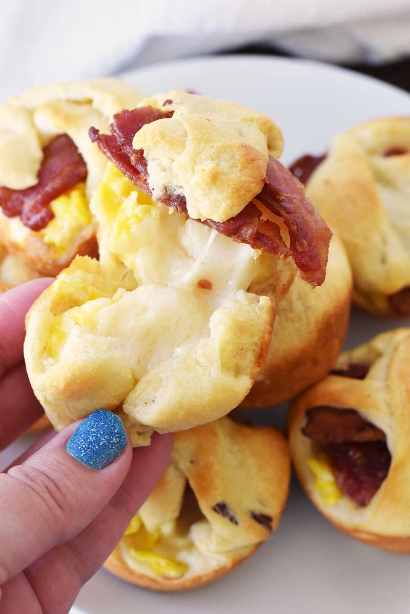 A hand with blue sparkle nail polish is pulling apart a bacon egg, and cheese crescent bite.