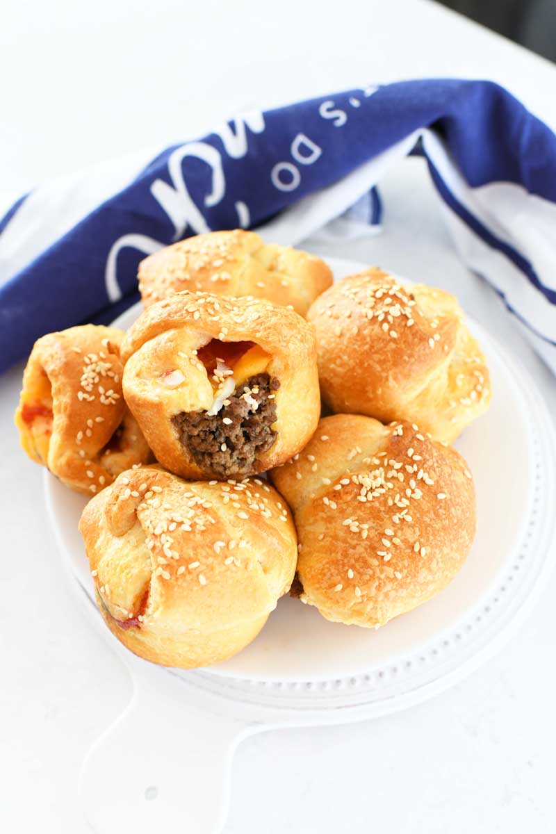 Crescent Cheeseburger Cups made in a muffin tin. They are on a white plate and there is a blue napkin in the background.