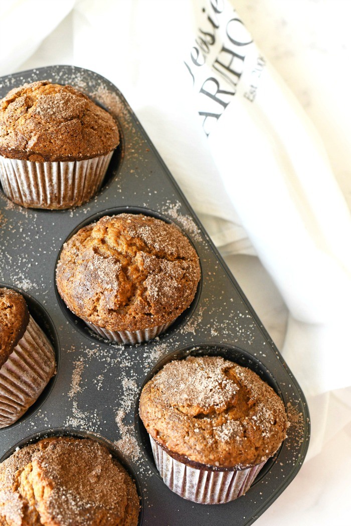 Jumbo Cinnamon + Sugar Pumpkin Muffins in a tin muffin pan. A white baking towel in nearby.