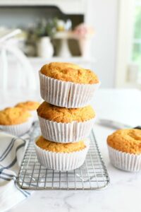 Jumbo Honey Corn Muffins stacked on a silver baking rack. There are two muffins also in this shot.