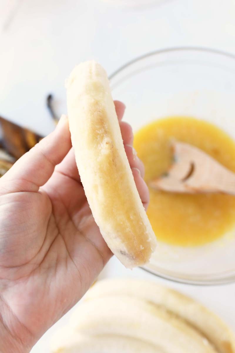 Over ripe jellied banana in someone's hand. There is a batter in a bowl on the table.