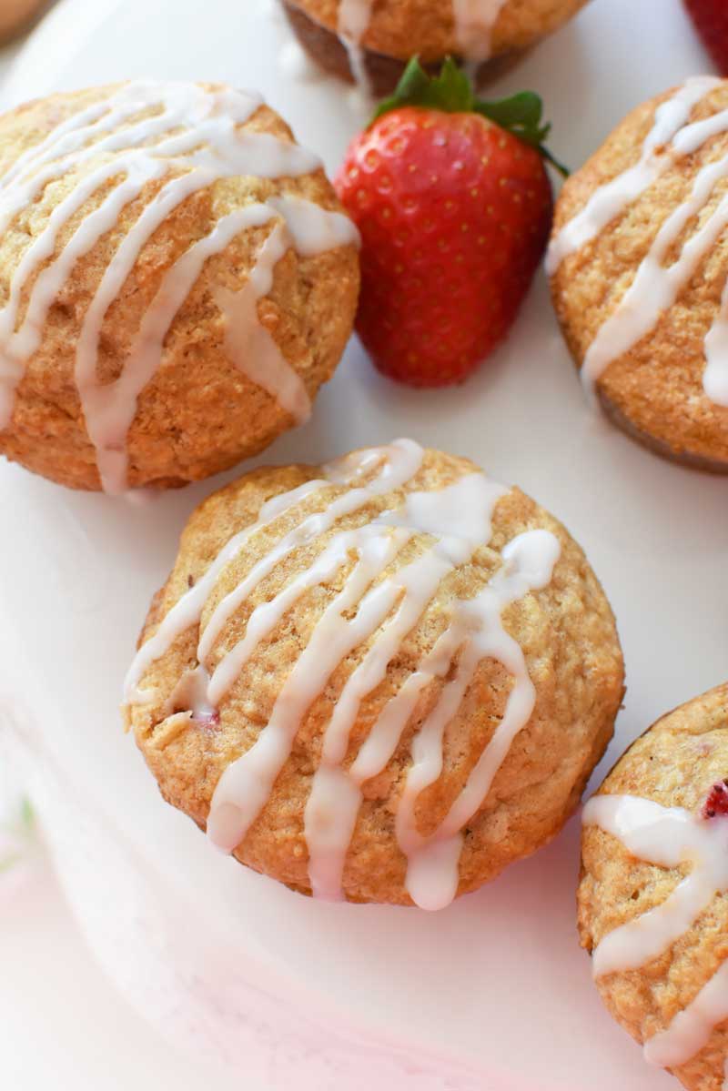 Iced Strawberry Muffins and fresh strawberries are on a white cake stand. 