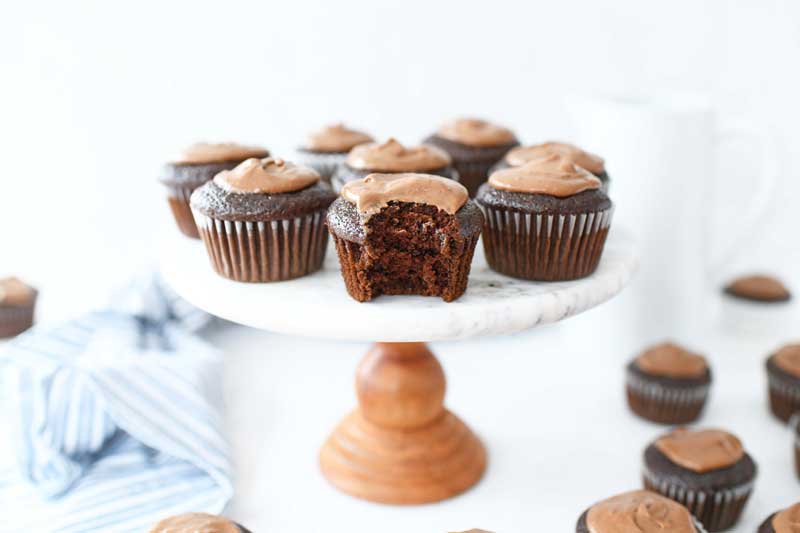 Chocolate Mayonnaise Cupcakes on a marble and wood stand. Once cupcake has a bite taken out. 
