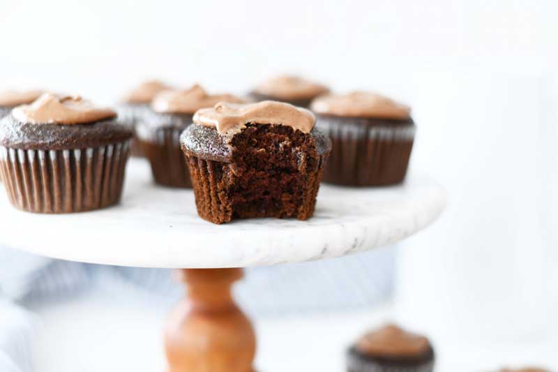 Chocolate Mayonnaise Cupcake with a bite taken out on a marble and wood cake stand. 