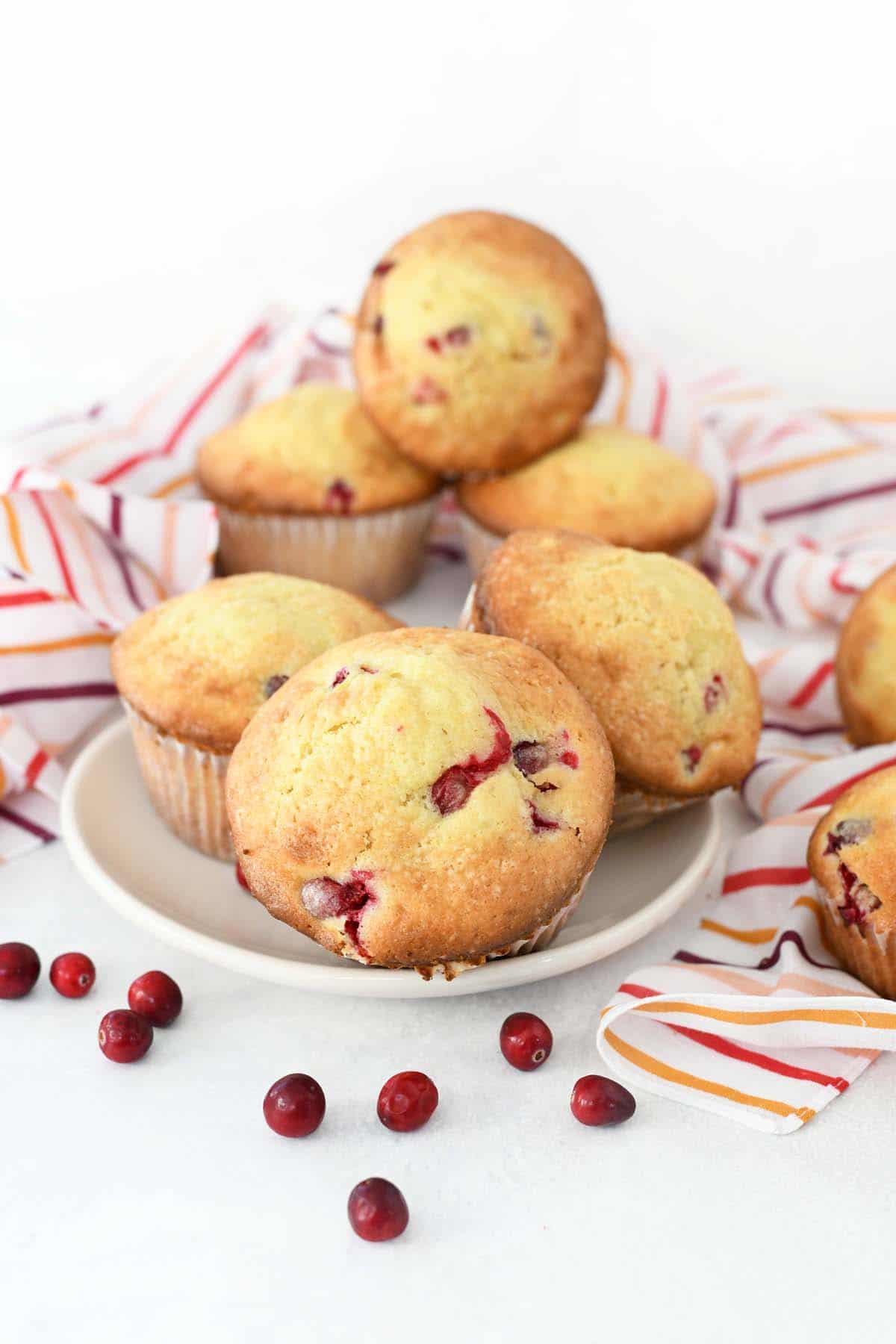 Cranberry Orange Muffins in a bowl with striped napkins and whole cranberries.