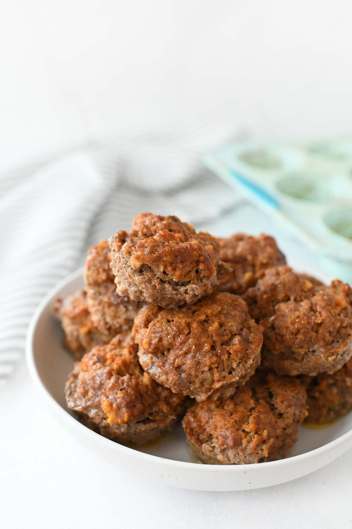 Meatloaf in a Muffin pan. These are all stacked on a white plate with a blue muffin pan in the background.