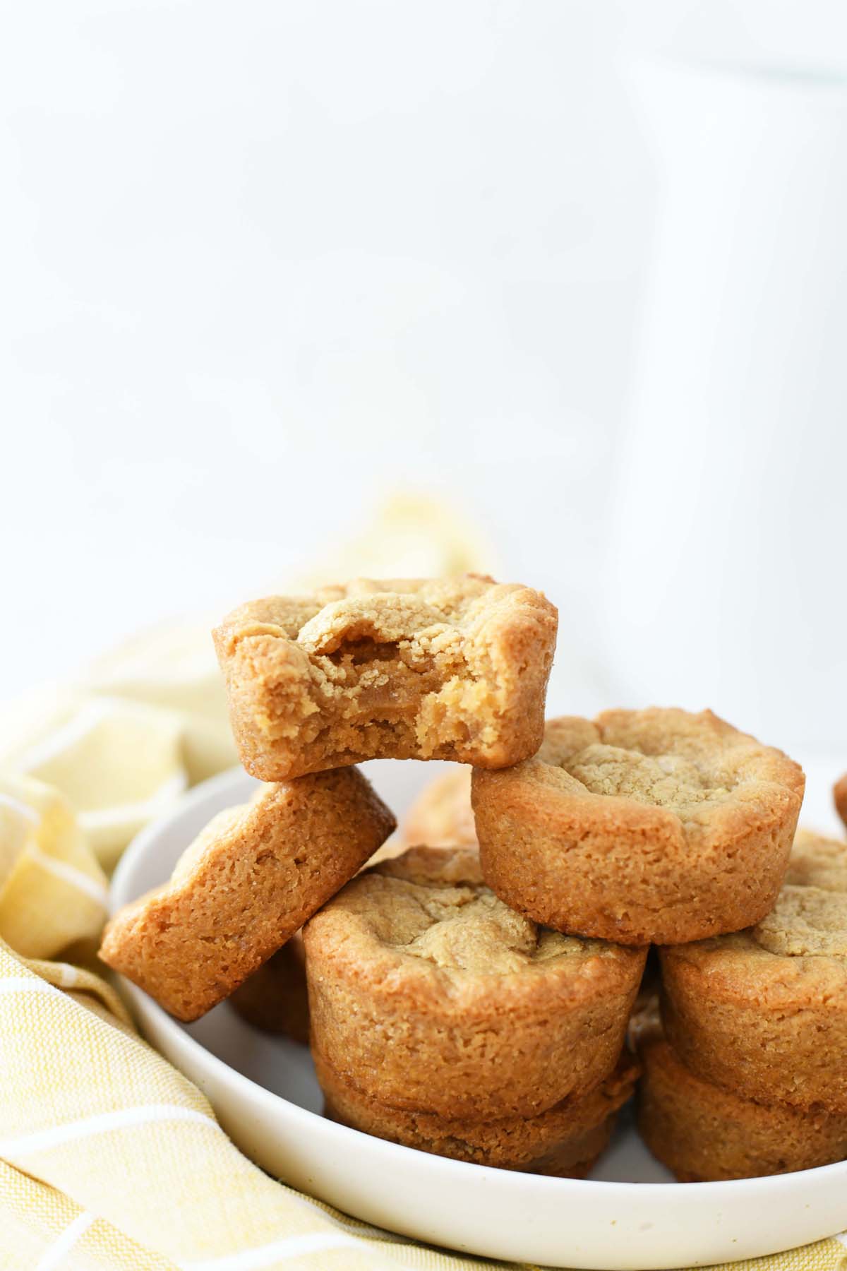 Muffin tin brownies made of peanut butter. These are on a white plate with a milk jug near it. 