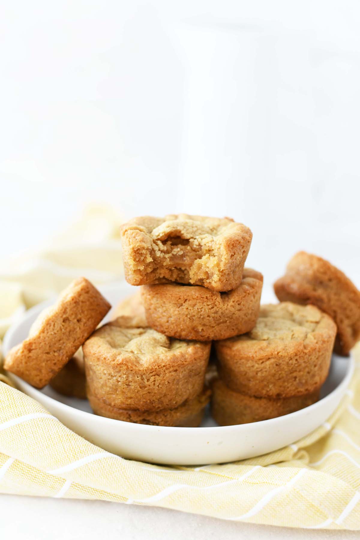 Muffin tin peanut butter brownies in a white bowl. There is a milk container, and a yellow napkin in this shot.