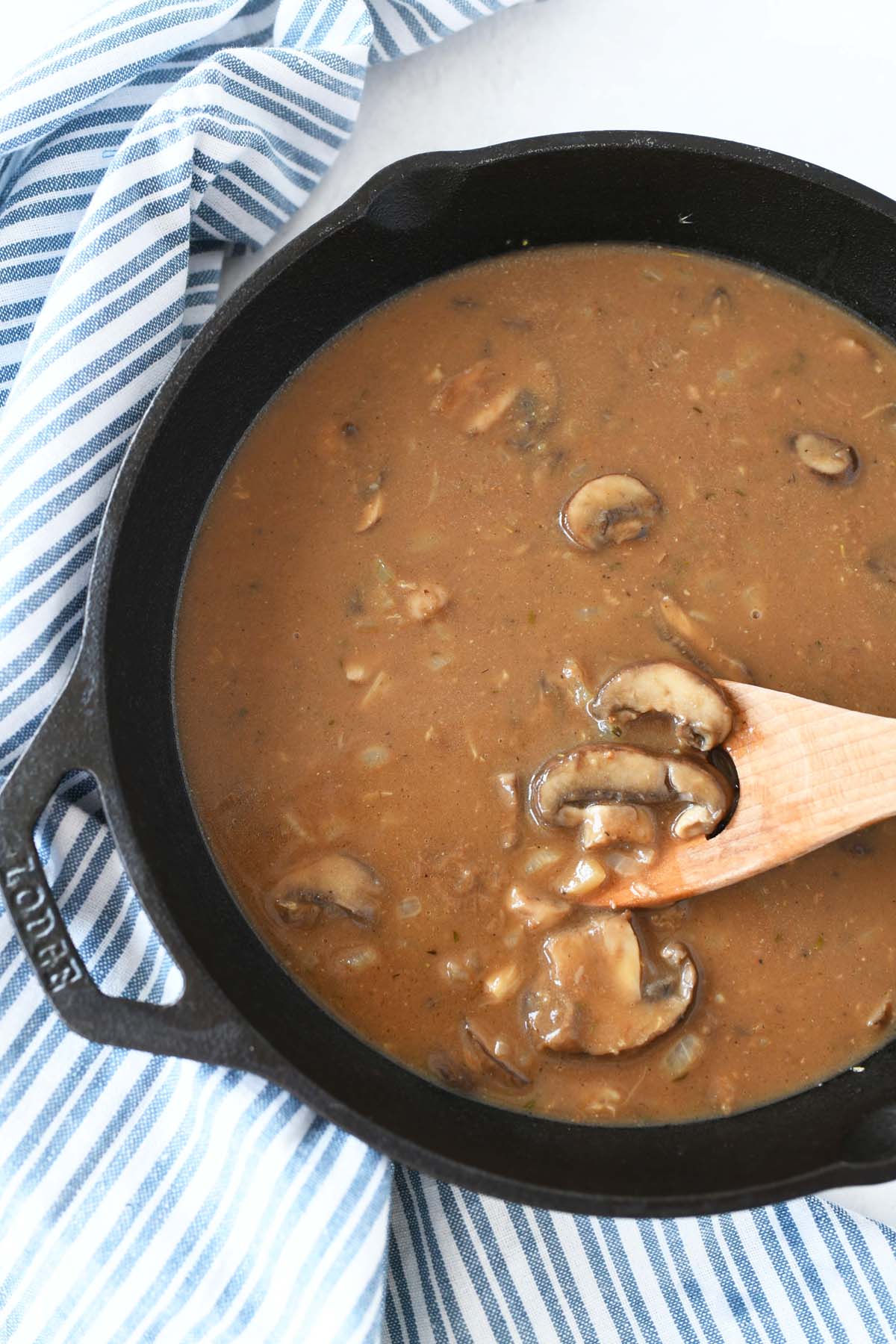 Mushroom Salisbury Steak Gravy in a black skillet with a blue striped napkin and a wooden spoon.