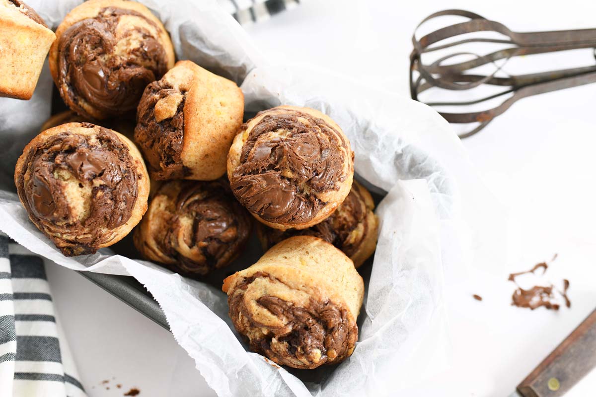 Nutella Banana Muffins with an old fashioned whisk. There is also a striped napkin nearby. 