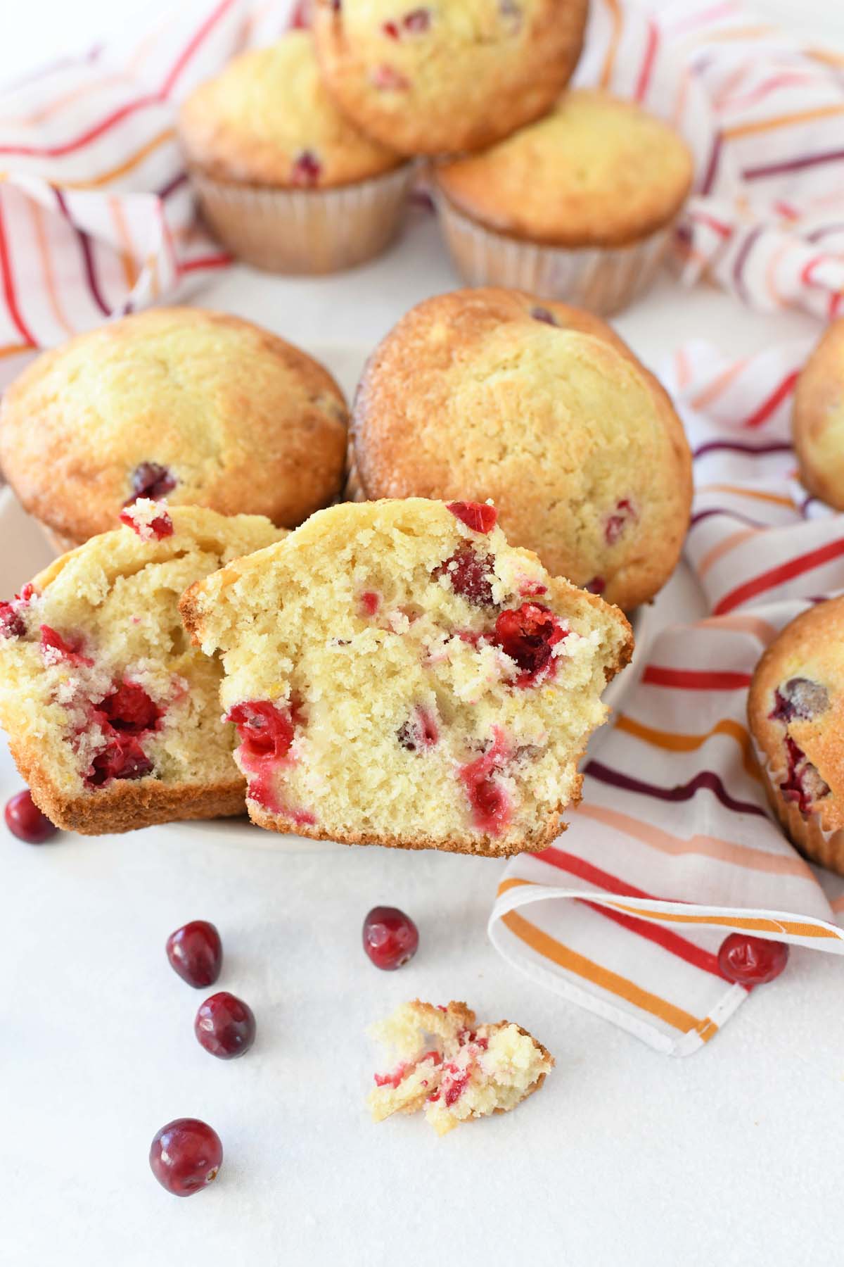 Orange Cranberry Muffins Recipe on a white table with cranberries and striped napkins.