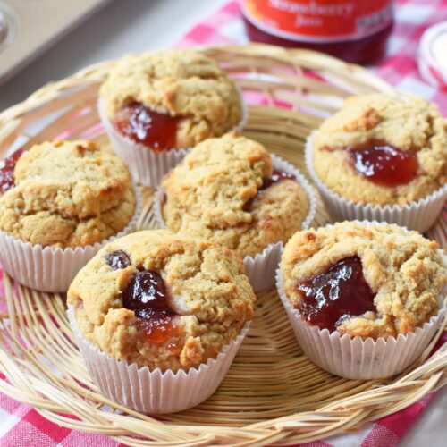 Peanut Butter and Jelly Muffin in a wicker basket with a red, plaid napkin. There is a jar of Smucker's Jam in the background.