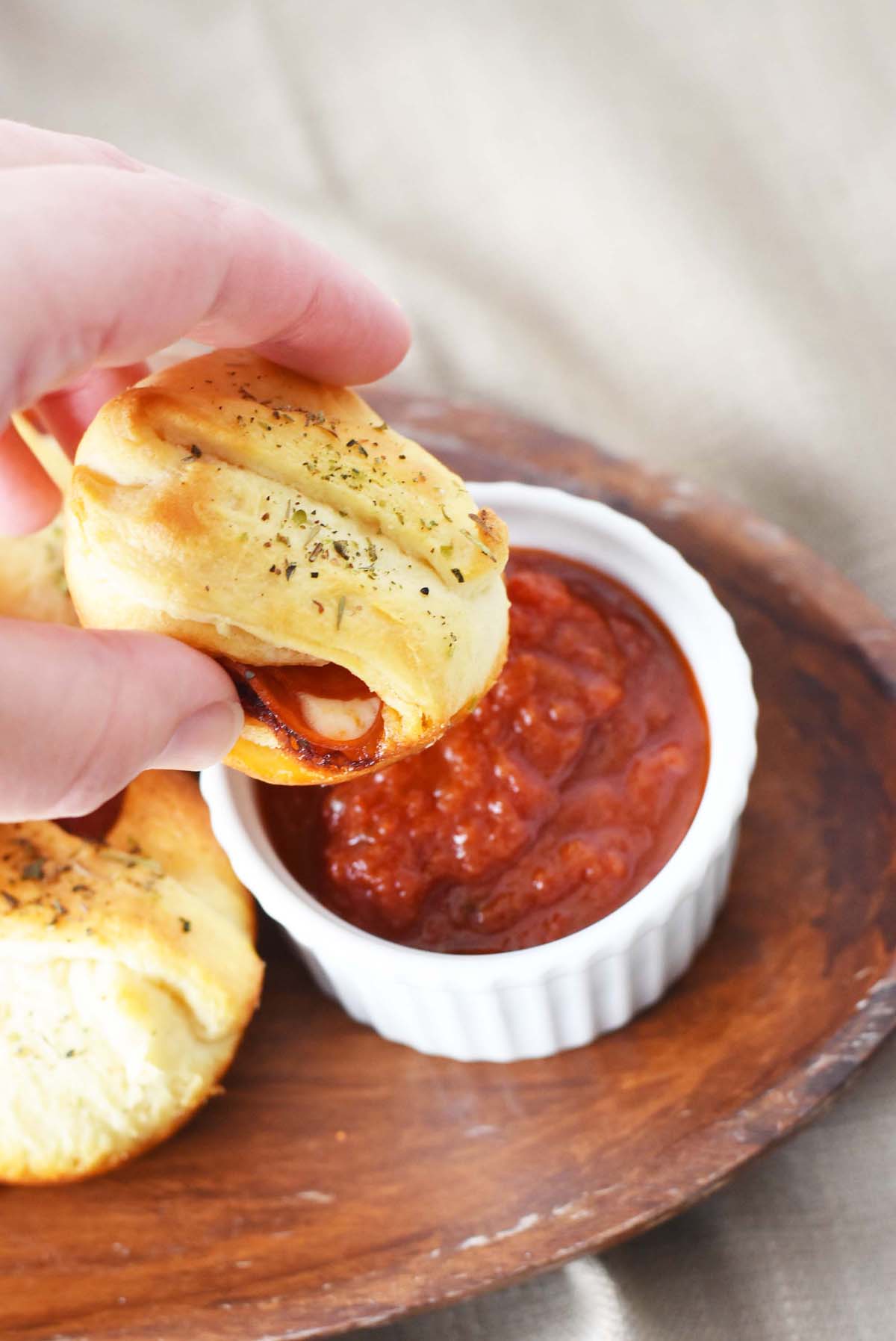 Pepperoni Cheese Pizza Bites being dipped in sauce on a wooden platter.