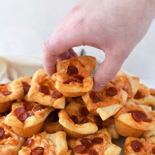 Pepperoni Pizza Crescent Bites on a platter. A hand is picking a bite up.