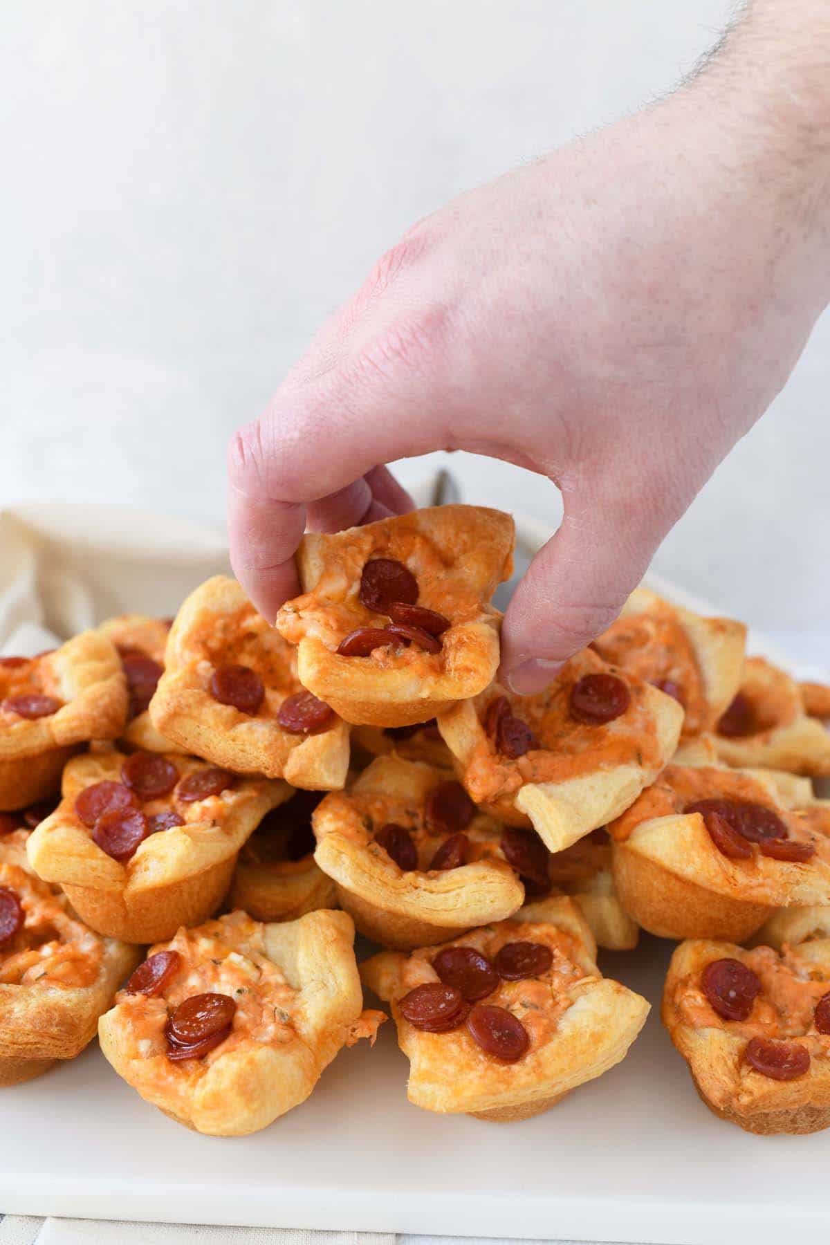 Pepperoni Pizza Crescent Bites on a platter. A hand is picking a bite up.