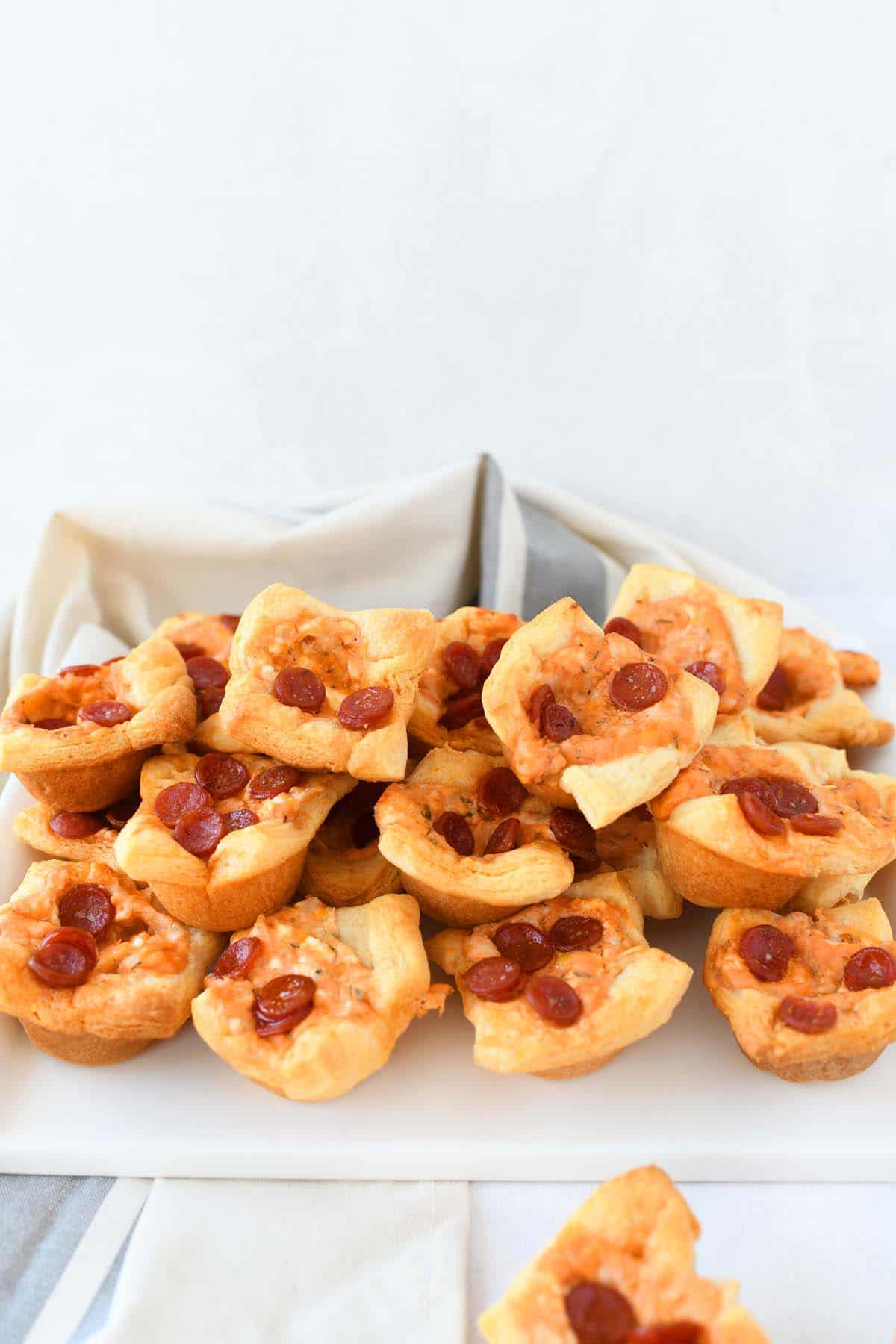 Pepperoni Pizza bites on a white tray with a tan napkin in the shot.