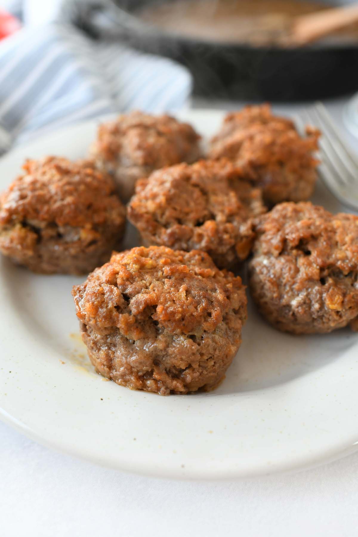 Salisbury Steak in Muffin Tin. An image of baked steak patties on a white plate with gravy in the background.