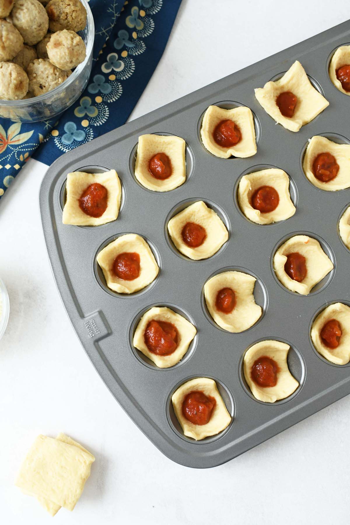 Crescent dough with marinara in a mini muffin tin.