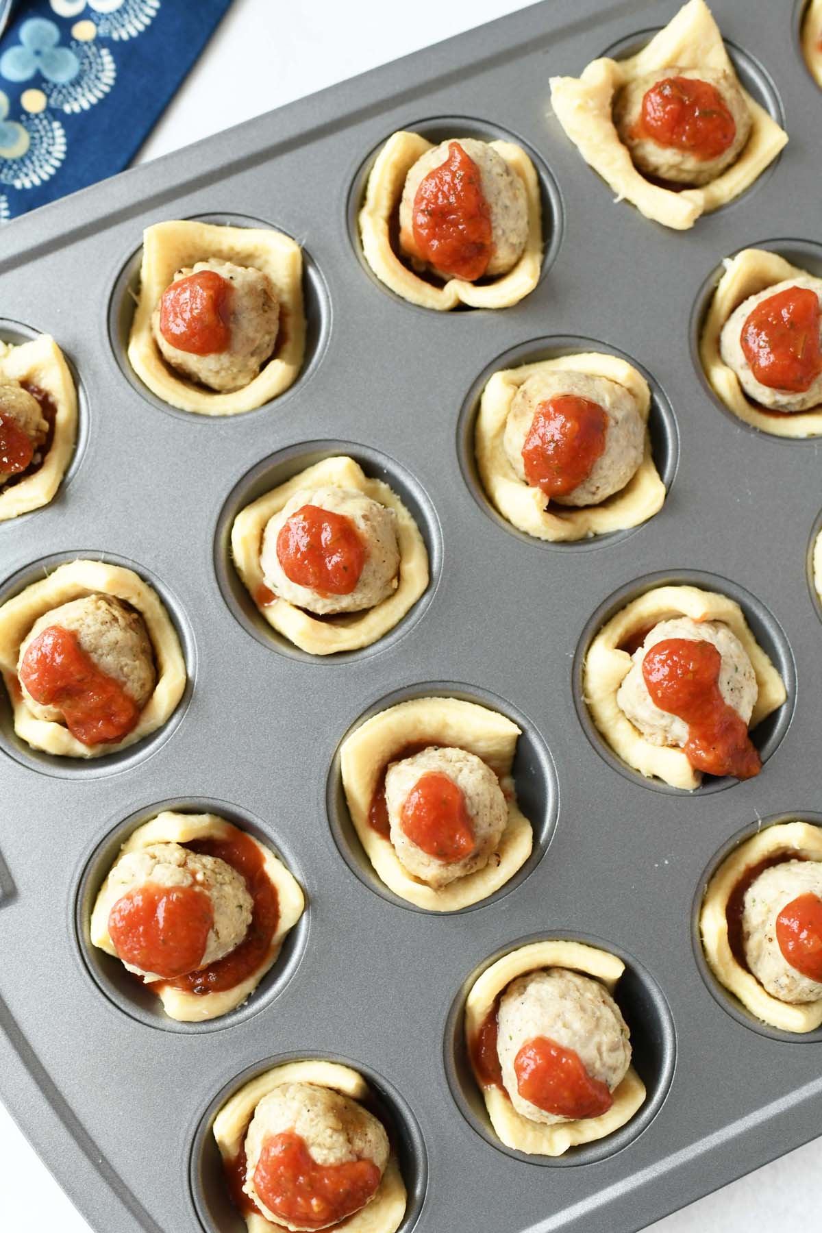 Meatballs in crescent dough with sauce in mini muffin tin.