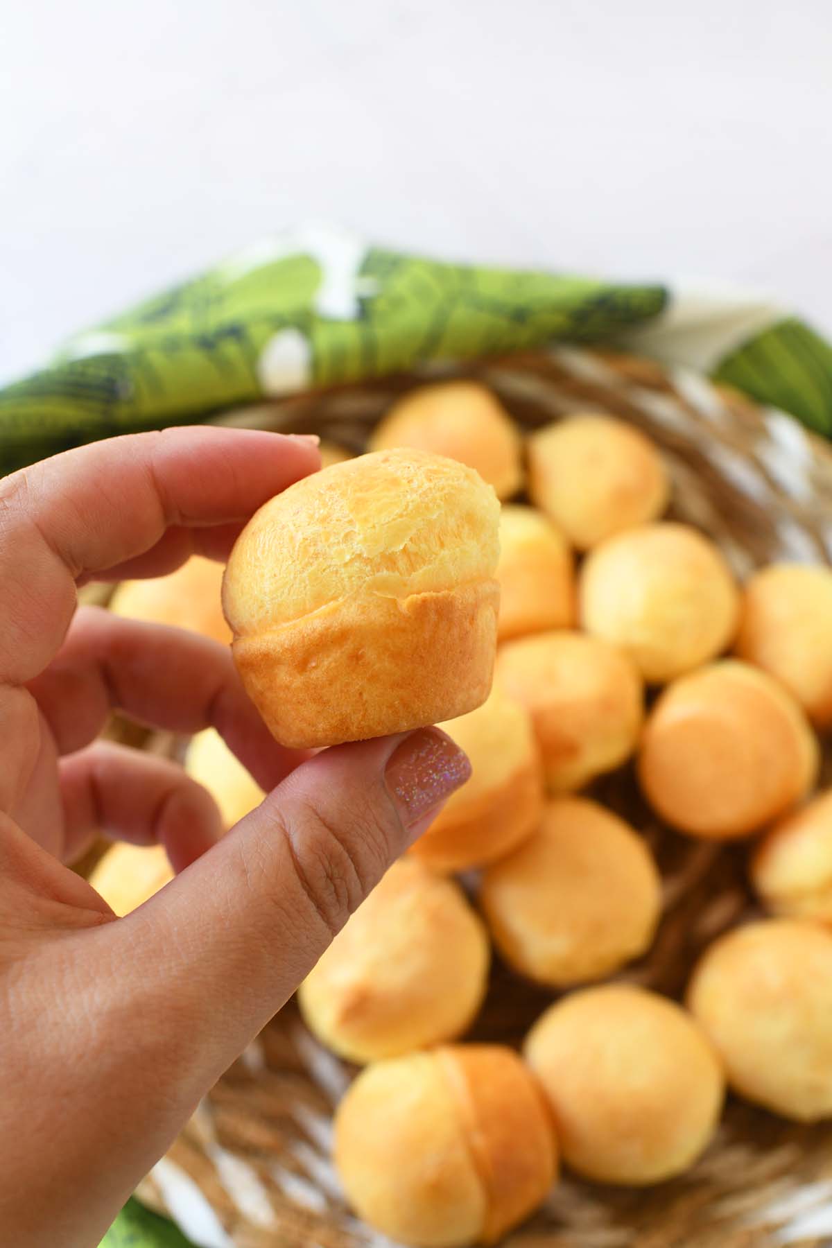 A hand holding up a mini, golden-brown Brazilian cheesebread.