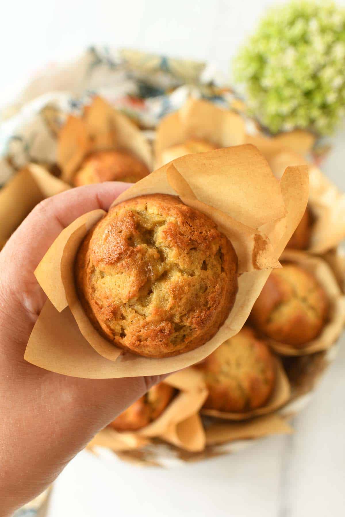 A hand holding up a fluffy banana muffin in a cupcake liner.