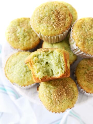 Jumbo Pistachio muffins on a white surface with a bite taken out of one.