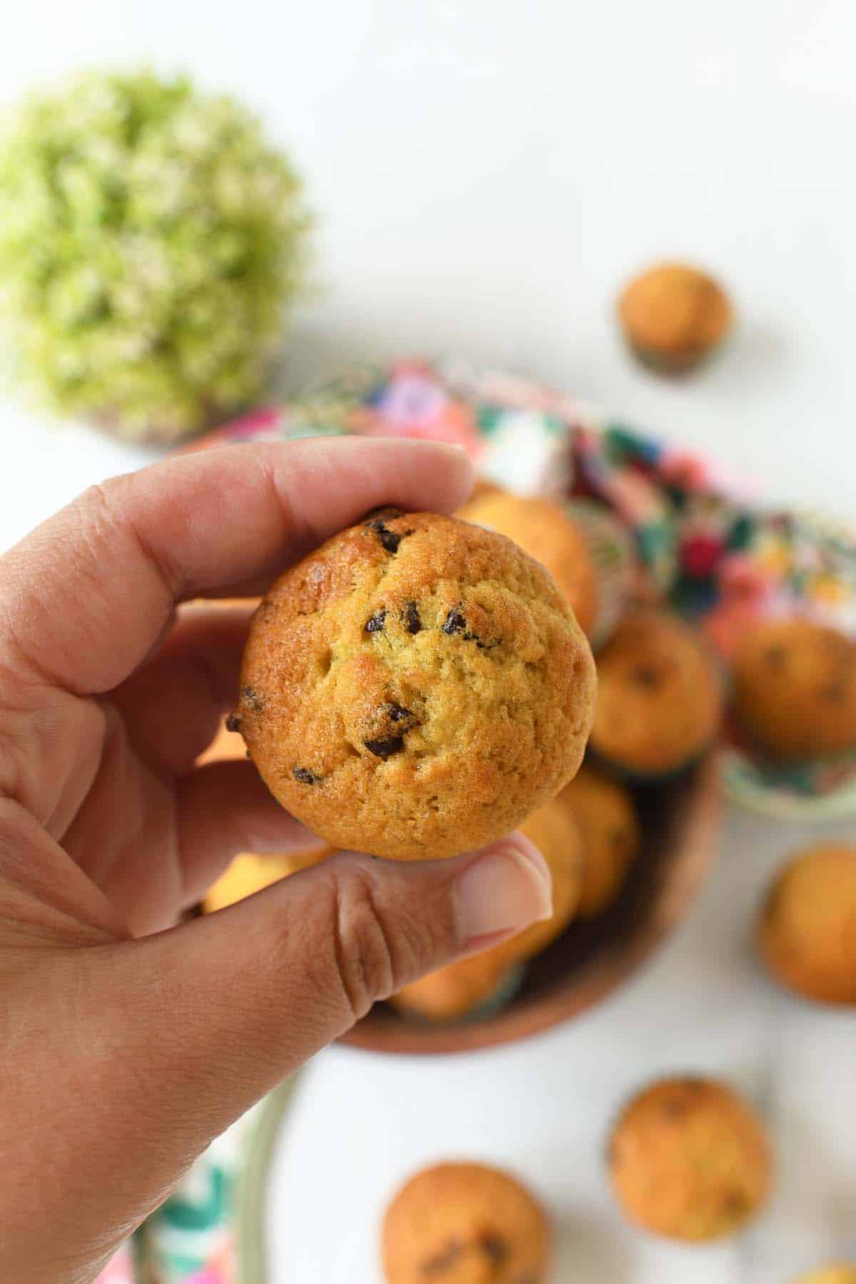 A hand holding up a mini chocolate chip banana muffin.
