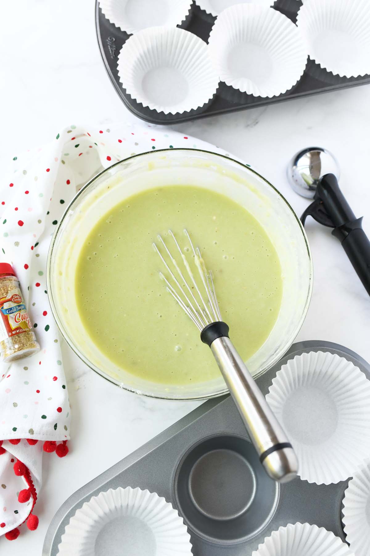 A bowl of green batter near a jumbo muffin tin with white liners.