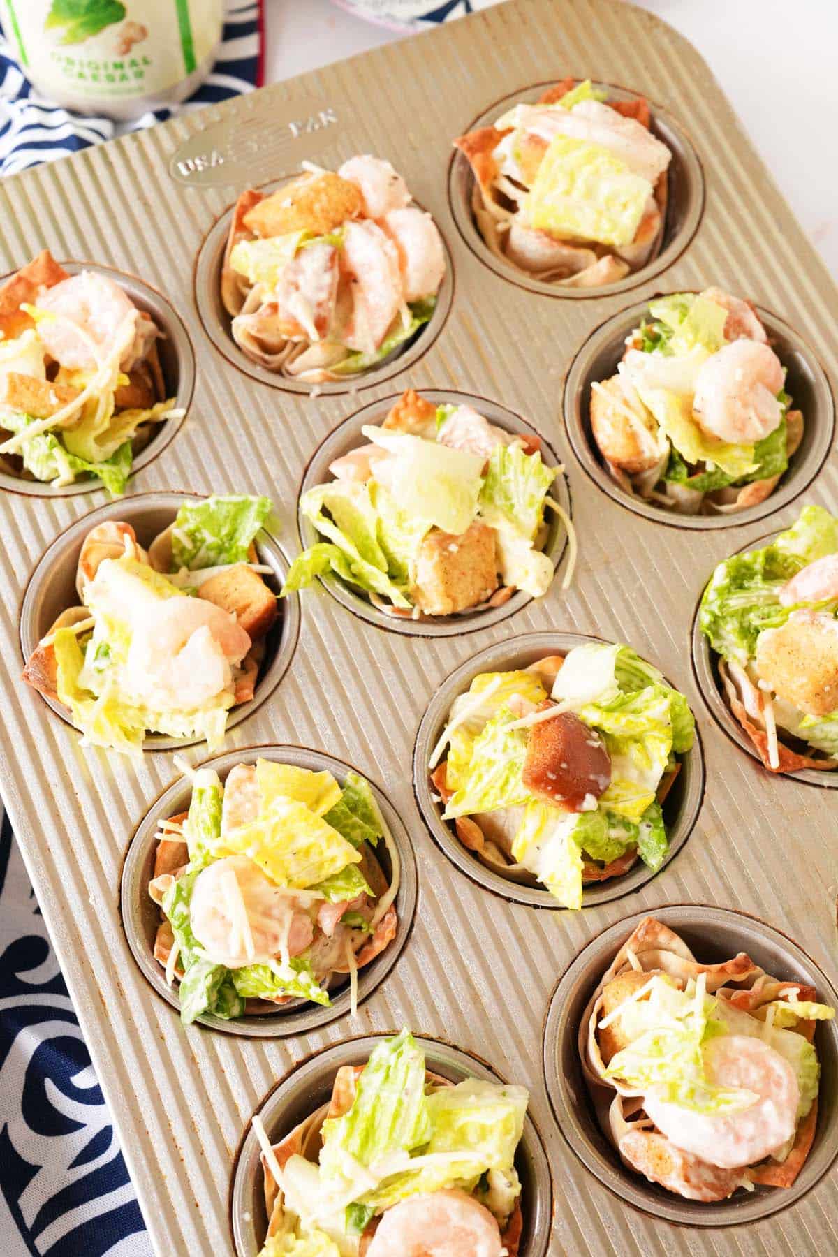 Assembled shrimp caesar salad wonton cups in a silver muffin tin.