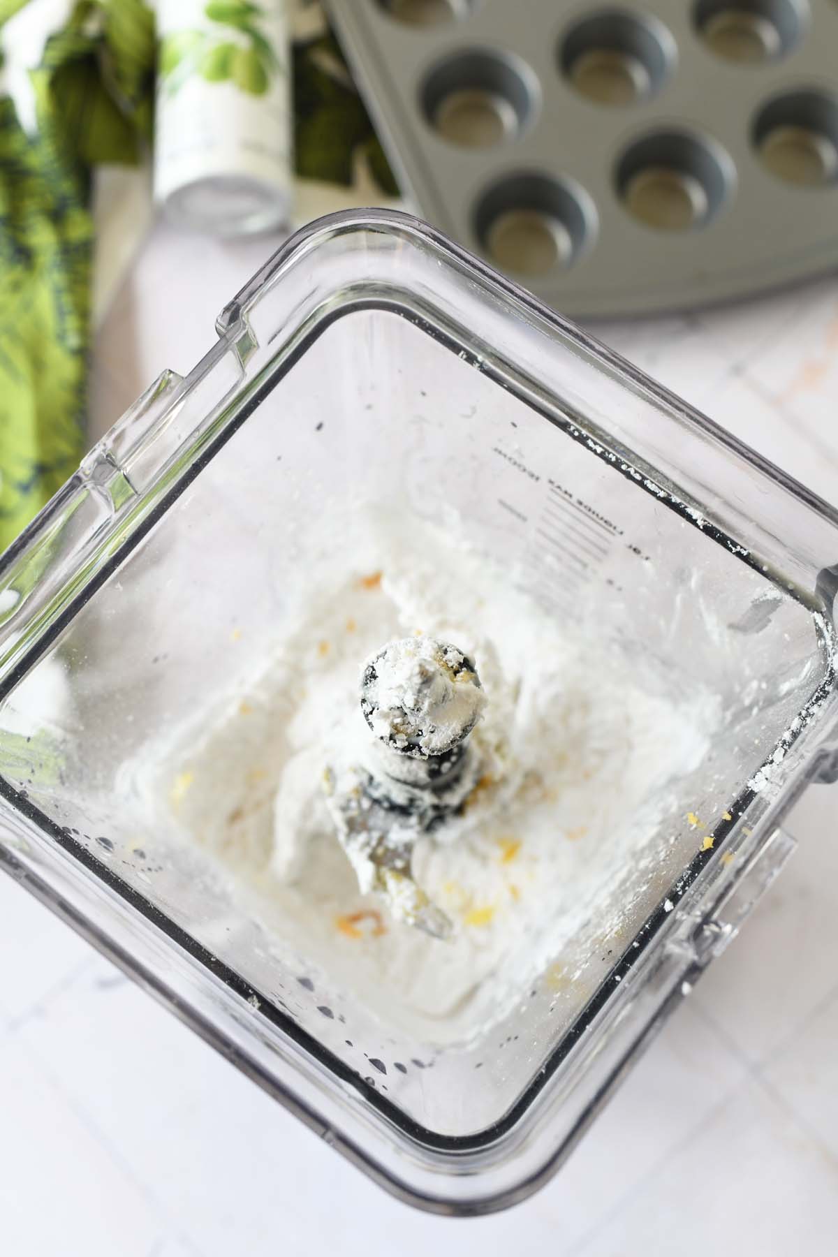 Brazilian cheesebread ingredients in a blender near a green napkin and muffin tin.