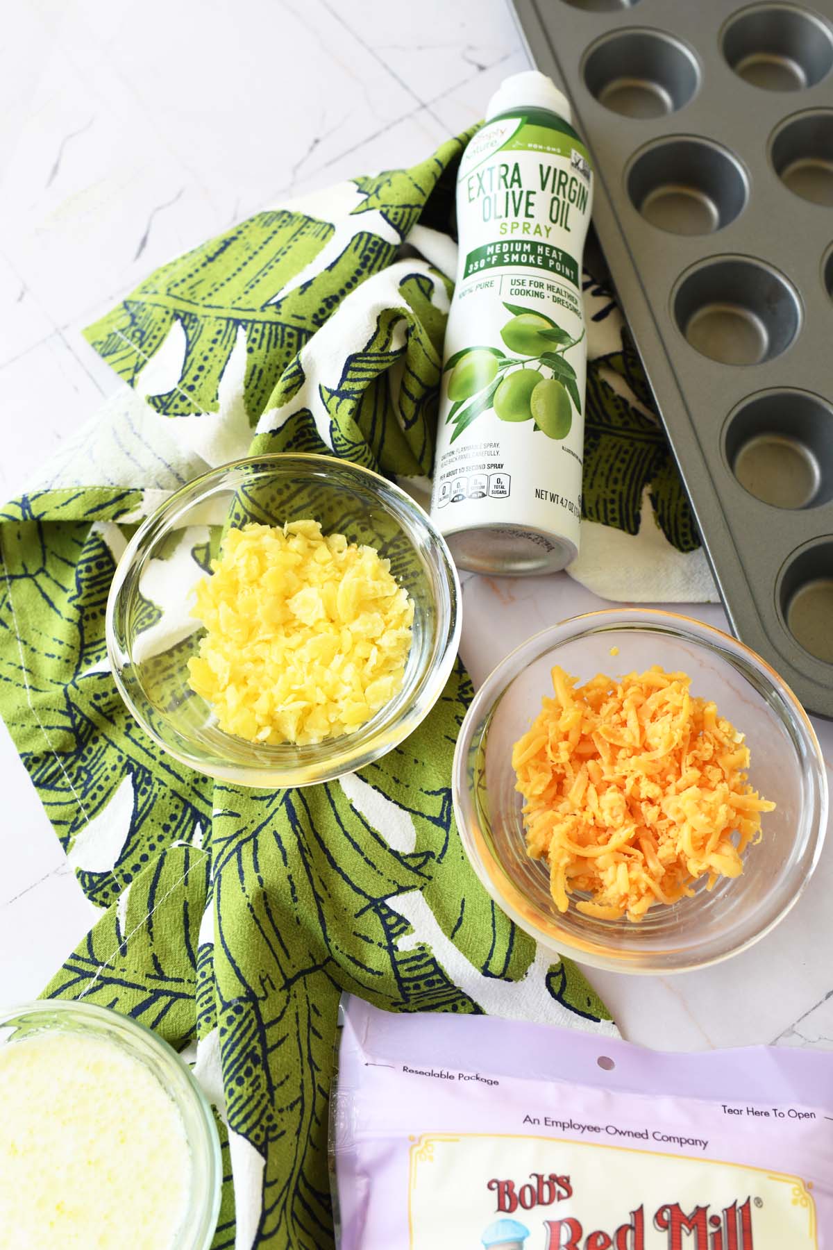 Shredded cheese in glass bowls with a muffin tin and green napkin nearby.