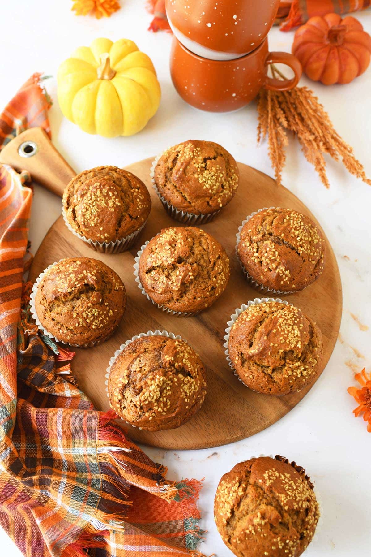 Jumbo bakery pumpkin muffins on a wooden platter, with fall decor nearby.