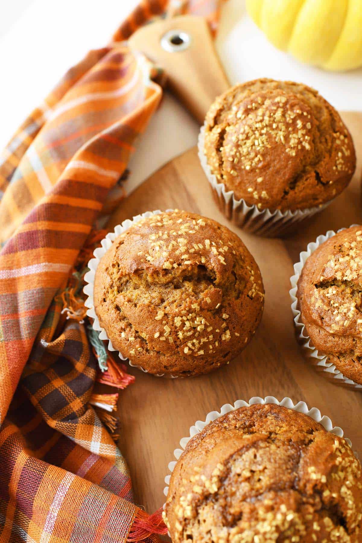 Jumbo pumpkin muffins with sanding sugar on top on a wooden platter with a fall napkin.